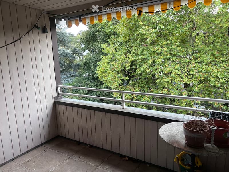 Balcony with wooden decking, white railing, and a small table with potted plants.