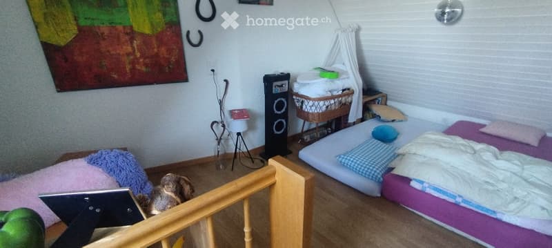 Cozy bedroom with a bed, nightstand, small table, and decorative items including a painting and a basket.