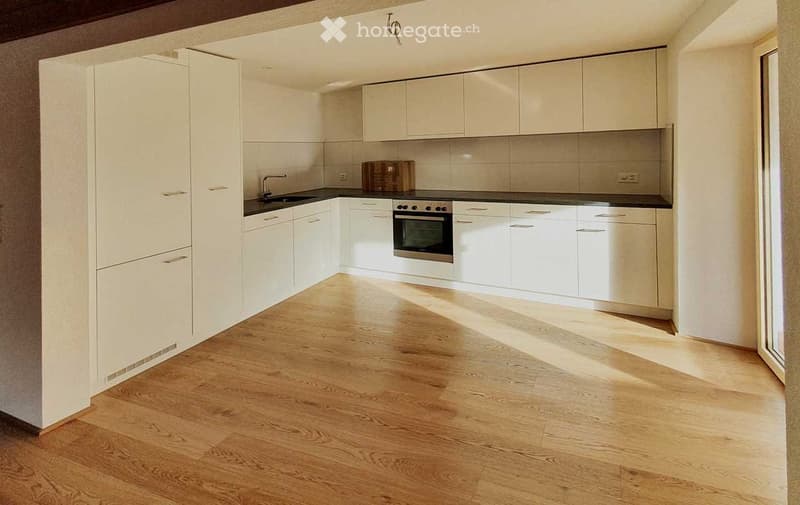 Modern kitchen with white cabinets, wooden flooring, and built-in appliances including a sink, oven, and faucet.