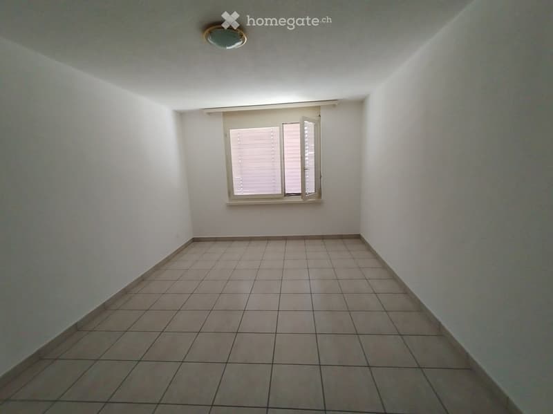 Empty room with tiled floor and white walls, featuring a window with blinds and a ceiling light fixture.