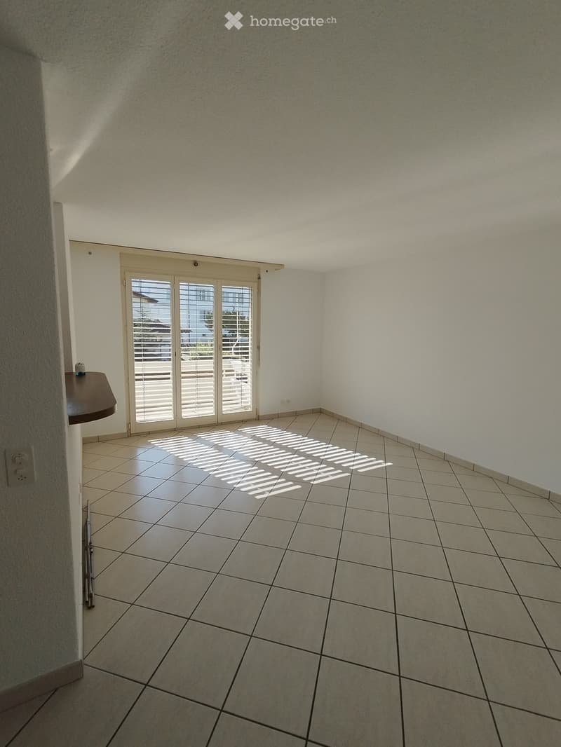 Empty room with tiled floor, white walls, and a sliding glass door with blinds leading to an outdoor area.