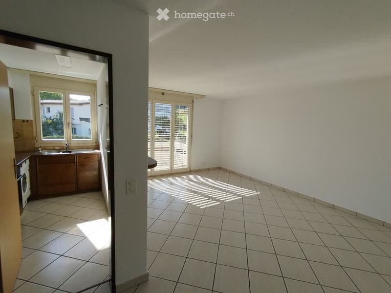 Empty room with tiled floor, white walls, and a doorway leading to another room with cabinets and a sink.