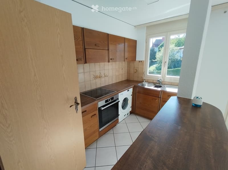 Modern kitchen with wooden cabinets, tiled backsplash, stainless steel sink, oven, washing machine, and a wooden countertop.