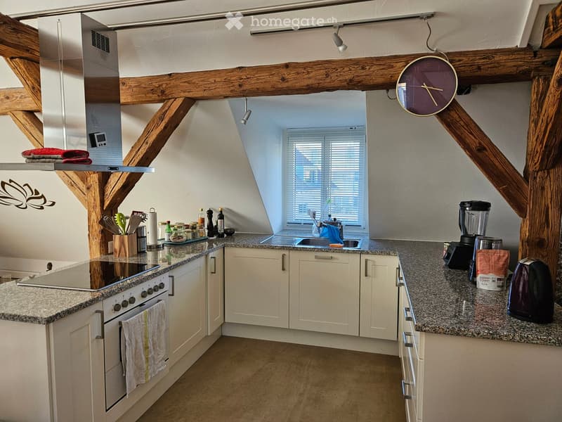 Modern kitchen with white cabinets, granite countertops, stainless steel appliances, and wooden beams on the ceiling.