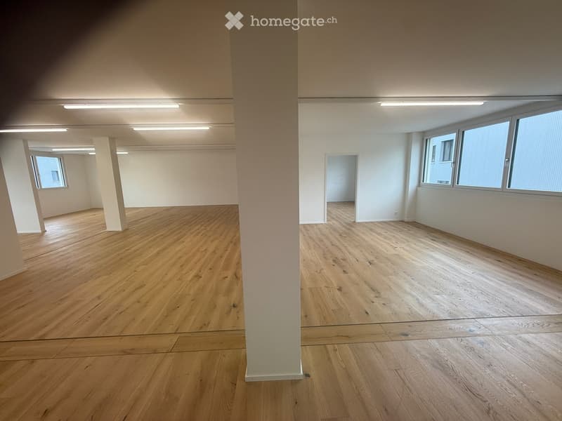 Empty room with wooden flooring, white walls, and large windows allowing natural light. No furniture or equipment present.