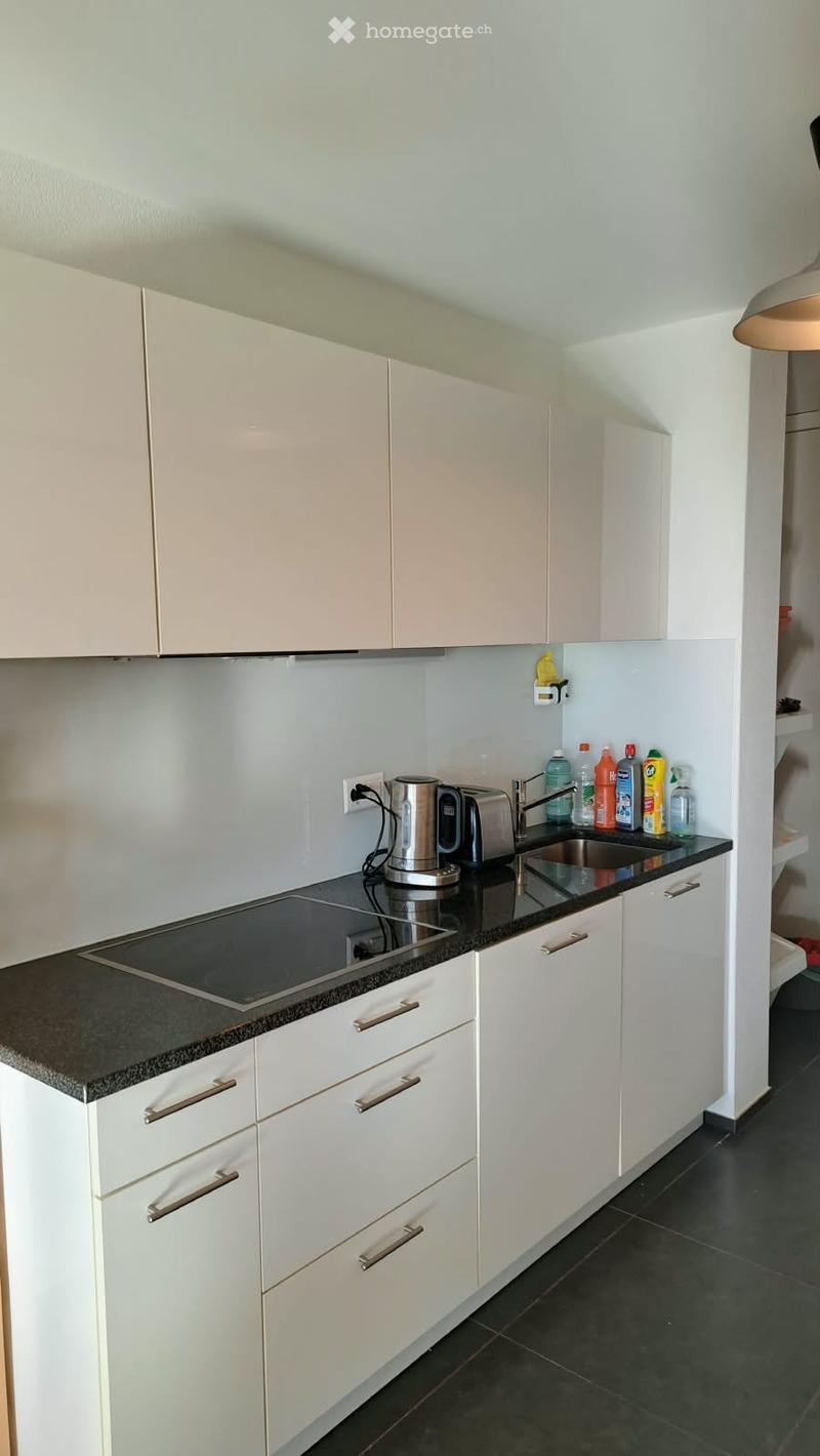 Modern kitchen with white cabinets, black granite countertop, induction cooktop, electric kettle, and various cleaning bottles on the counter.