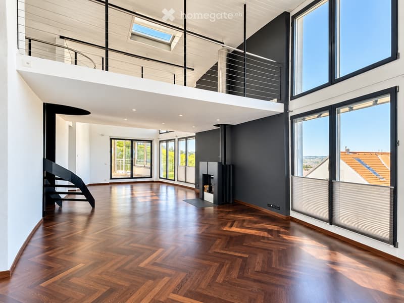 Modern, spacious living area with dark walls, wooden herringbone flooring, large windows, and a modern fireplace. Features a curved staircase leading to an upper level.