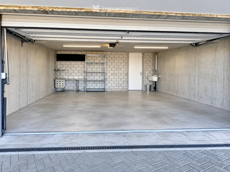Modern garage with concrete walls, tiled backsplash, shelving, sink, and storage units.