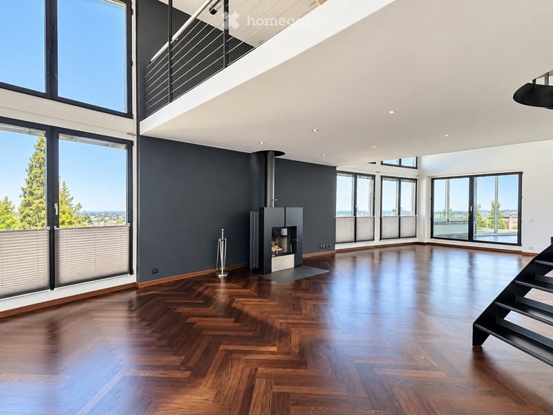 Open-concept unfurnished room with dark grey walls, polished wooden herringbone flooring, large windows and sliding glass doors offering a scenic view, and a modern fireplace with a black surround.