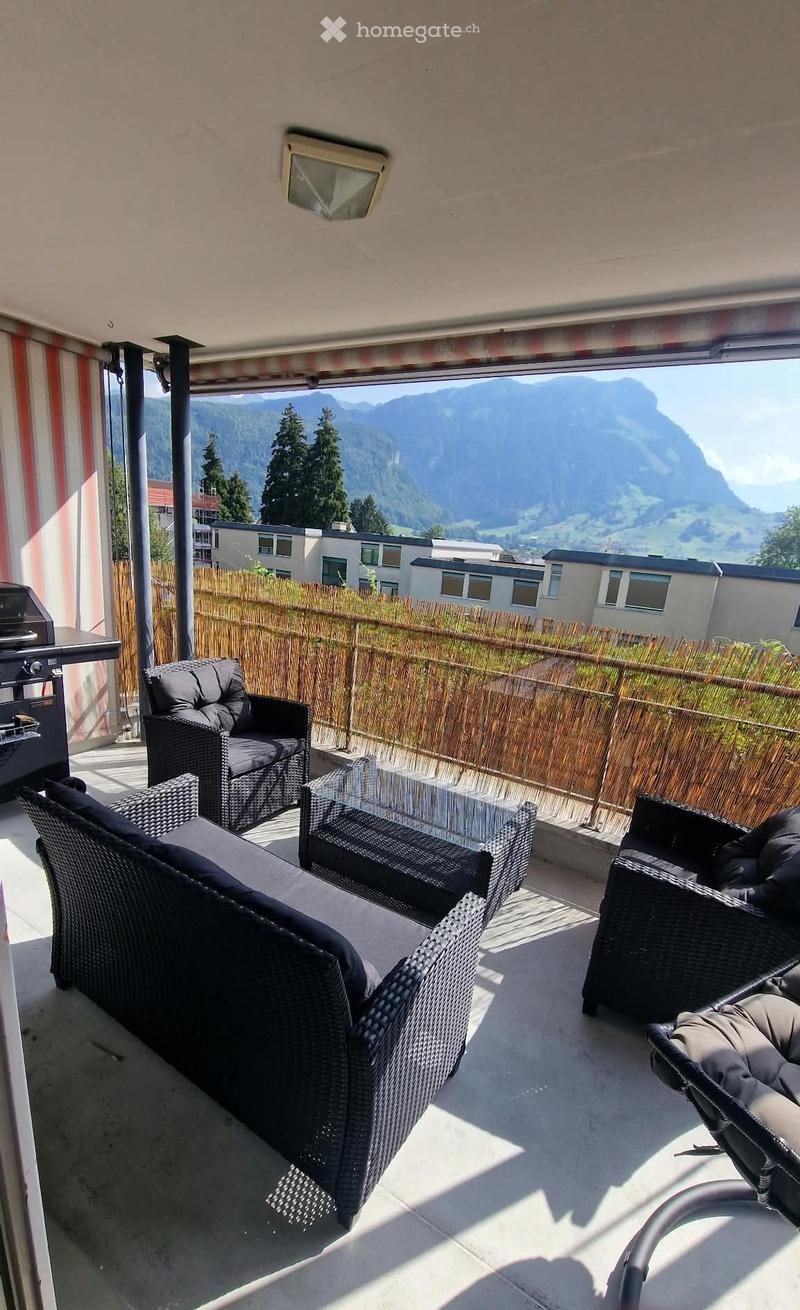 Balcony with wicker furniture, glass table, and scenic mountain view.