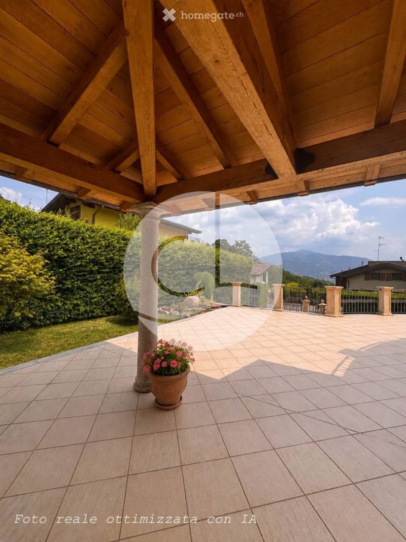 A spacious outdoor patio with a wooden pergola, tiled floor, and a view of the surrounding greenery and mountains.