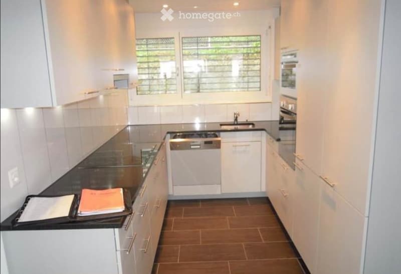 Modern kitchen with white cabinets, black countertop, stainless steel appliances, and a window with blinds.