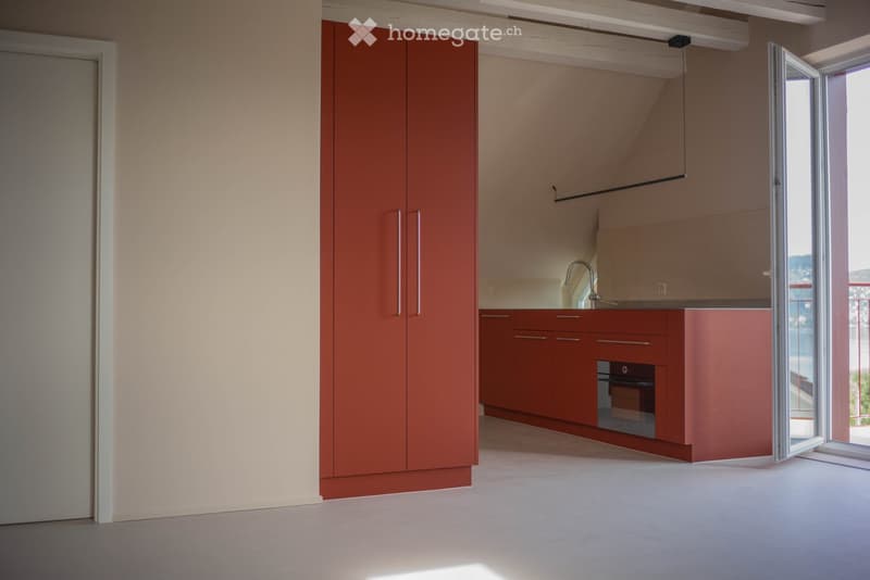 Modern kitchen with red cabinets, a sink, a faucet, and an oven, featuring a large window and a sliding door leading outside.
