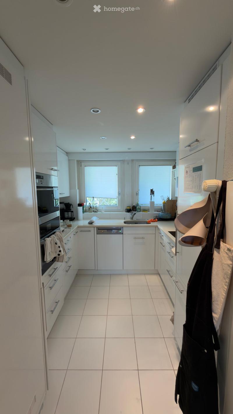 Modern kitchen with white cabinets, stainless steel appliances, and a central island. Features include a refrigerator, oven, dishwasher, and a sink with a window above it.