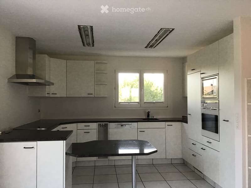 Modern kitchen with white cabinets, black countertops, built-in oven, microwave, and range hood. Features a central island with a black countertop and a sink with a modern faucet.