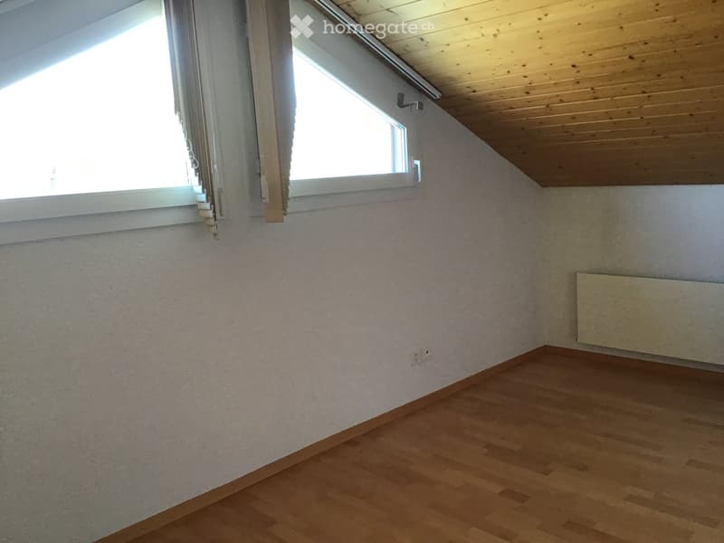 Empty room with wooden flooring, white walls, and two windows with blinds. A radiator is mounted on one wall.