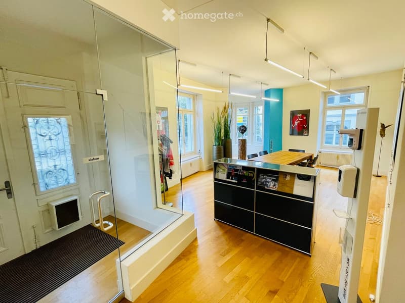 Modern office space with wooden flooring, reception desk, chairs, table, vase, and artwork on the wall.