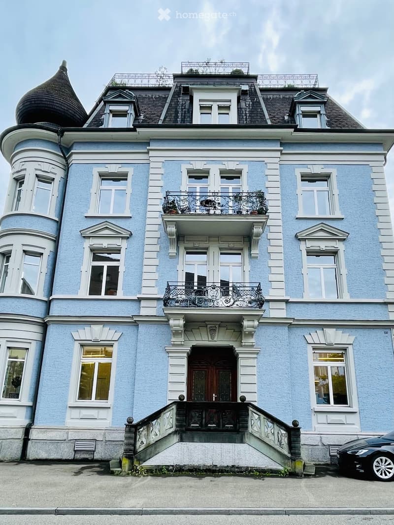 A three-story light blue house with white trim, multiple windows, balconies, and a decorative roofline.