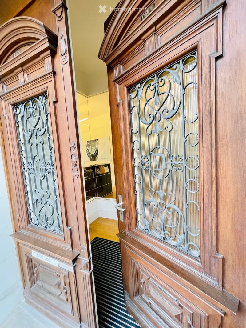 Ornate wooden doors with decorative metal grilles lead into a hallway with wooden flooring and a striped runner.