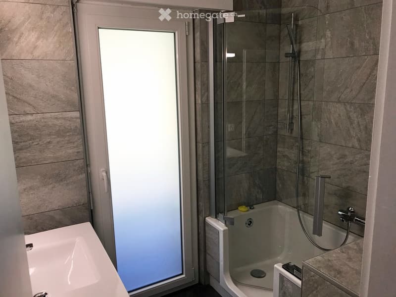 Modern bathroom with a bathtub, glass-enclosed shower, and a large window providing natural light.