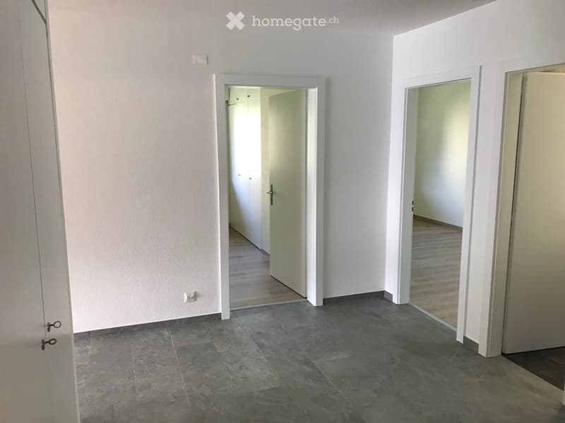 Empty hallway with grey tiled floor, white walls, and two open doors leading to other rooms.