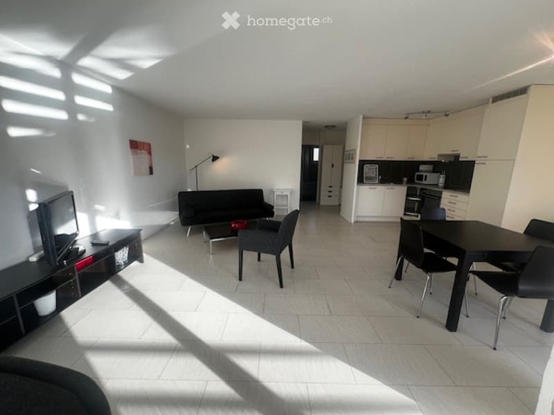 Living room with white tiled floor, black furniture, white cabinets, a microwave, a television on a stand, a desk, and a lamp