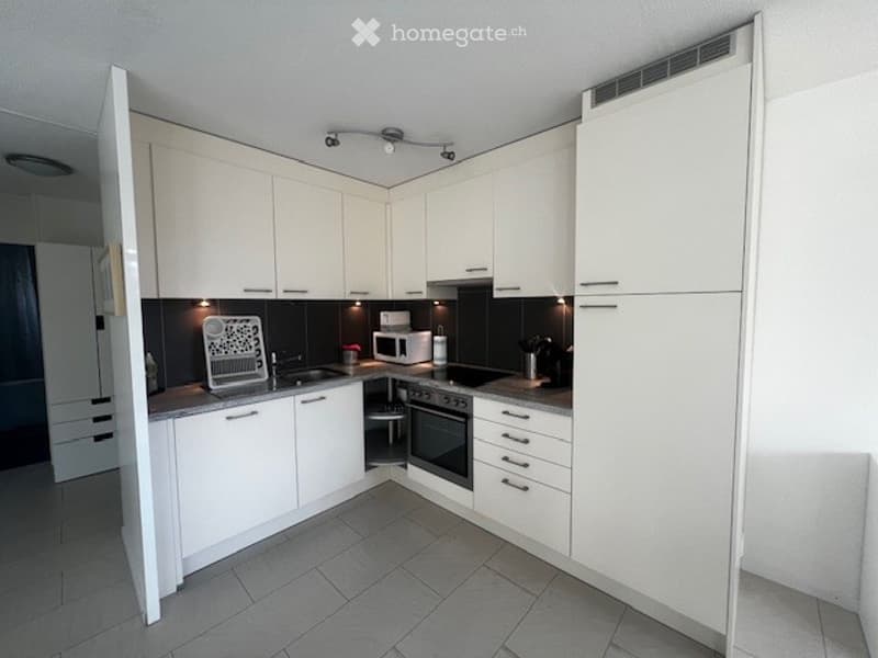 Modern kitchen with white cabinets, gray tiles, built-in appliances like dishwasher and microwave