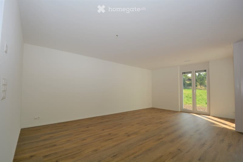 Empty room with wooden flooring, white walls, and large sliding glass doors leading to a green outdoor area.