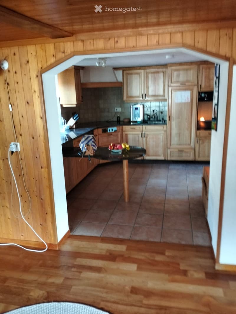 A modern kitchen with wooden cabinets, a black countertop, and a tiled floor. The kitchen features a sink, microwave, and a small table with a fruit bowl.