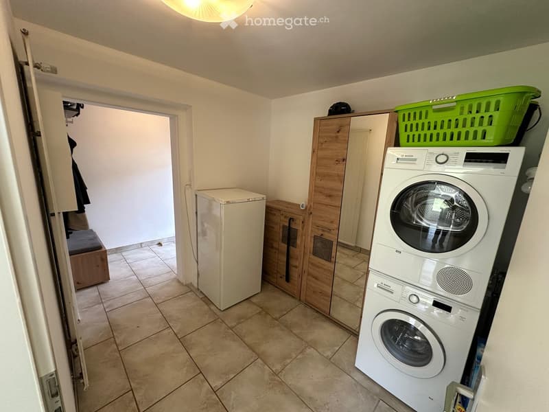A small bathroom with a washing machine and dryer stacked, a refrigerator, wooden cabinets, and a green basket on top of the cabinets.