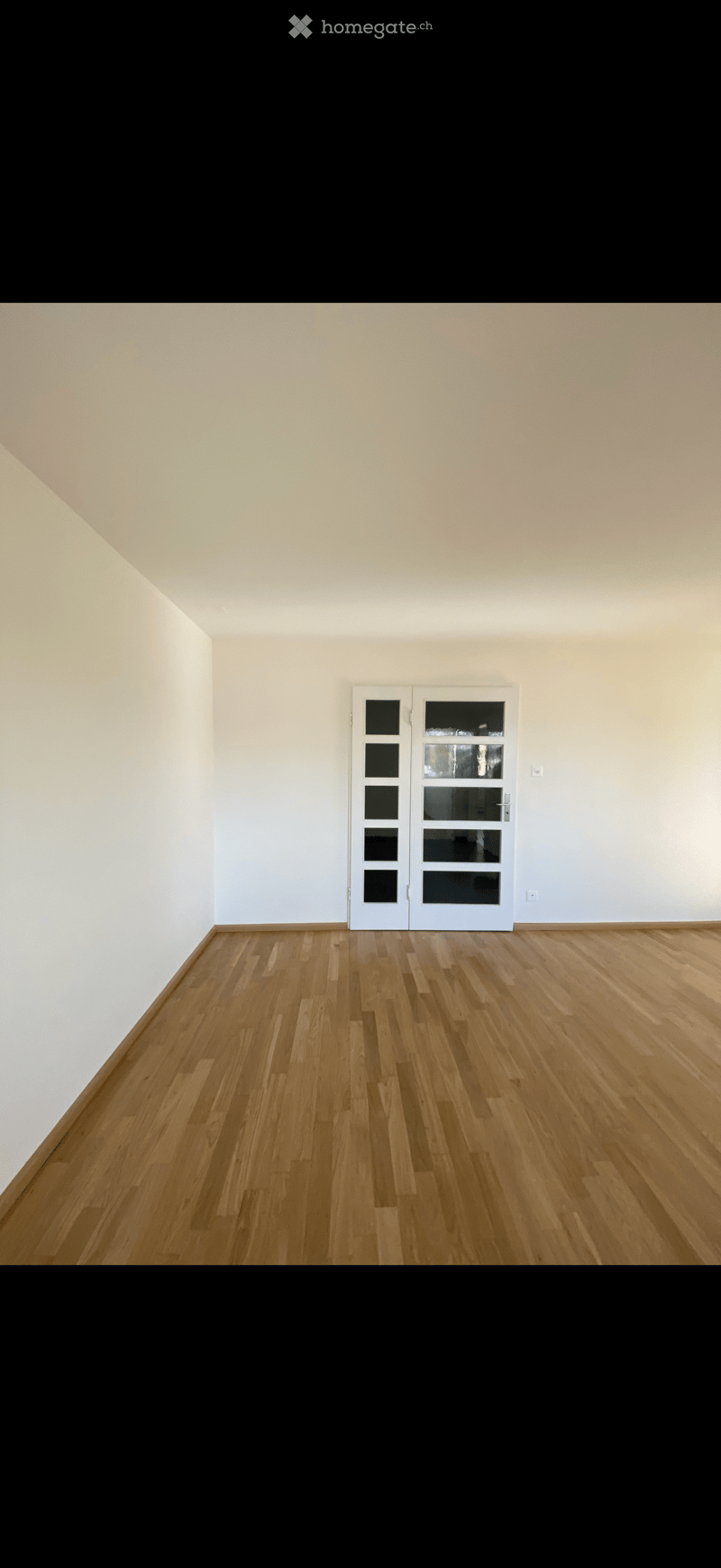 Empty room with light wooden flooring and white walls, featuring a white door with glass panels.