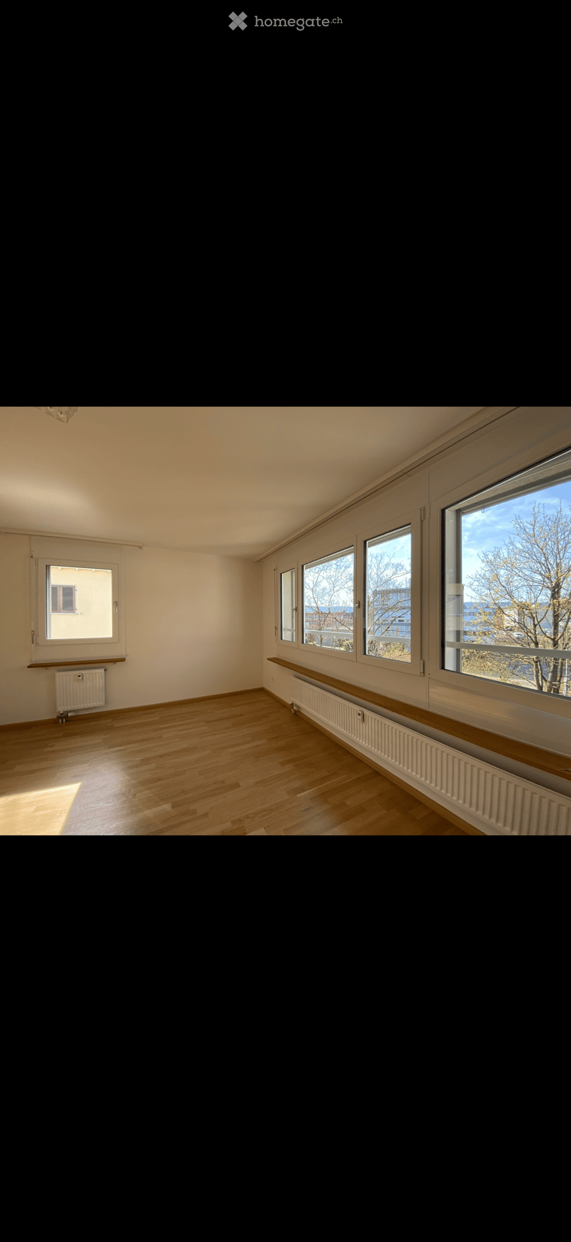 Empty room with wooden flooring, white walls, and large windows with radiators beneath them.