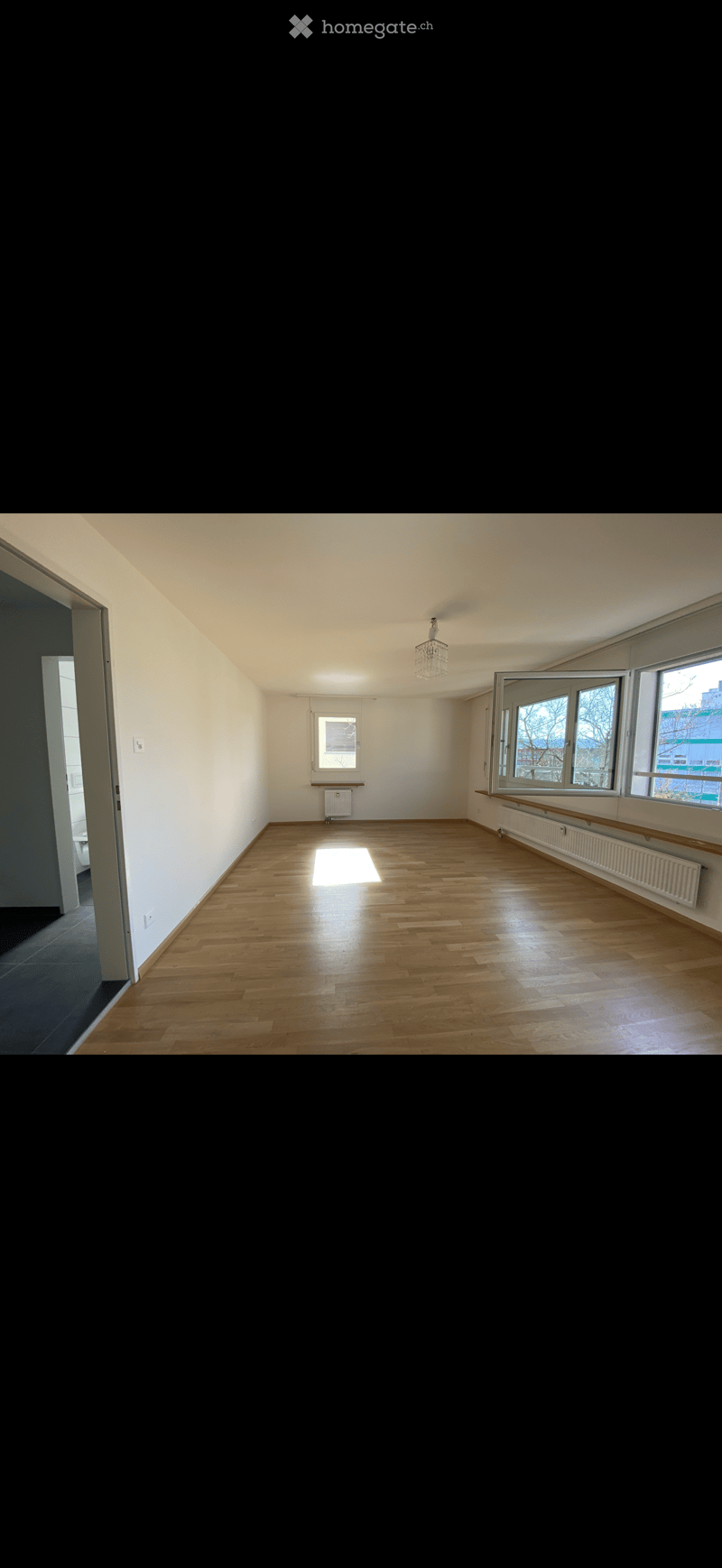 Empty room with wooden flooring, white walls, large windows, and a chandelier light fixture.