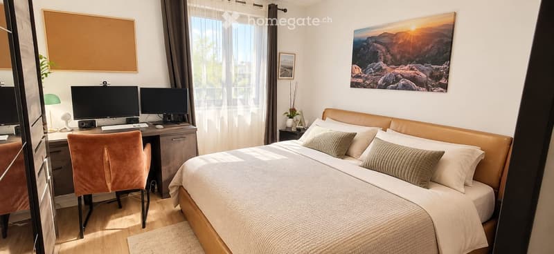 Cozy bedroom with a large bed, desk with two screens, a chair, and decorative artwork on the walls.