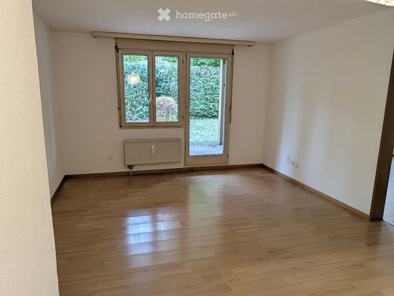 Empty room with wooden flooring, white walls, and large windows with blinds. A radiator is mounted on one wall.