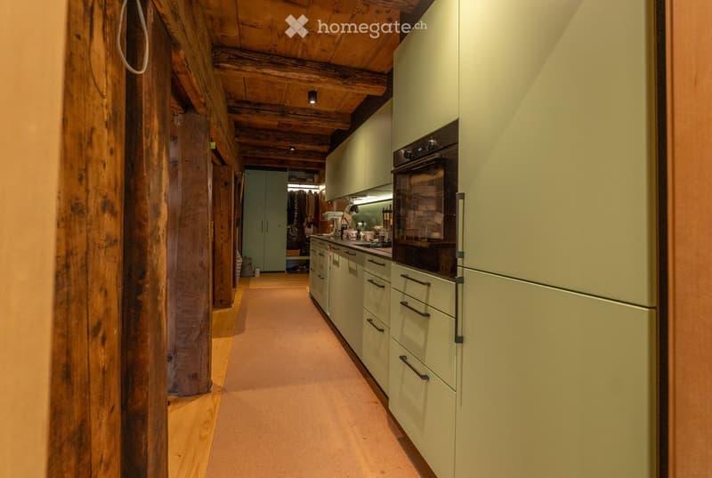Modern kitchen with light green cabinets, stainless steel oven, and wooden beams on the ceiling.