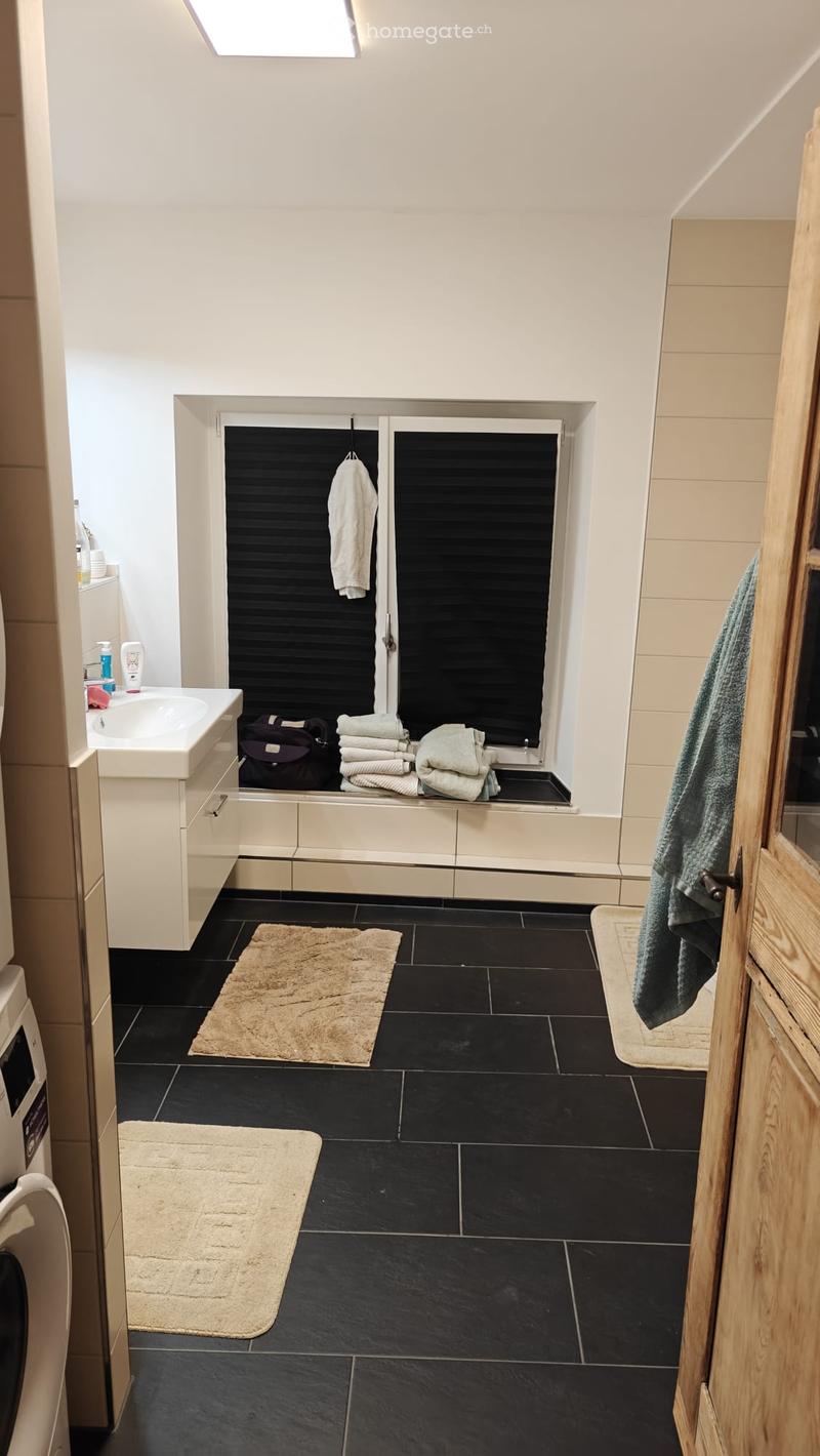 Modern bathroom with black tiled floor, white walls, a sink with a cabinet, a mirror, towels, and a small window with blinds.