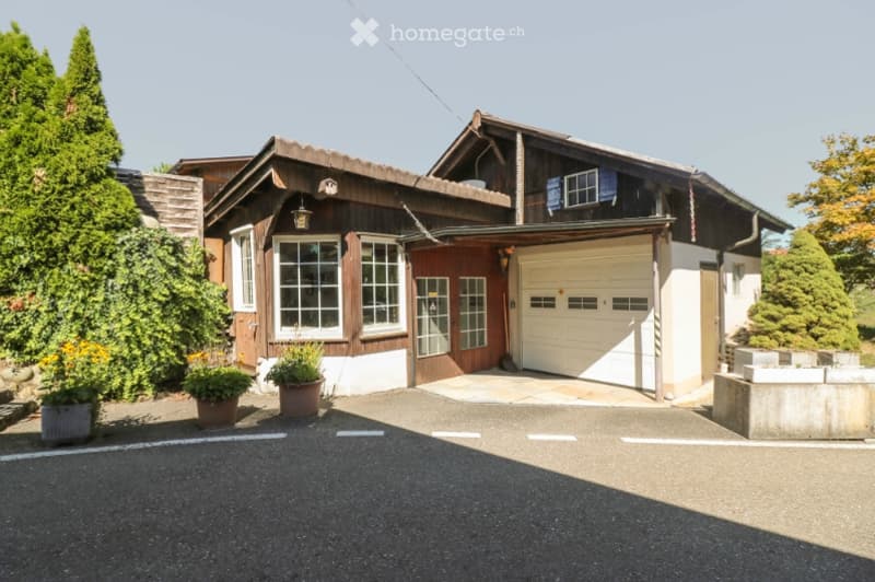 Two-story wooden house with a garage, multiple windows, and a well-maintained exterior.