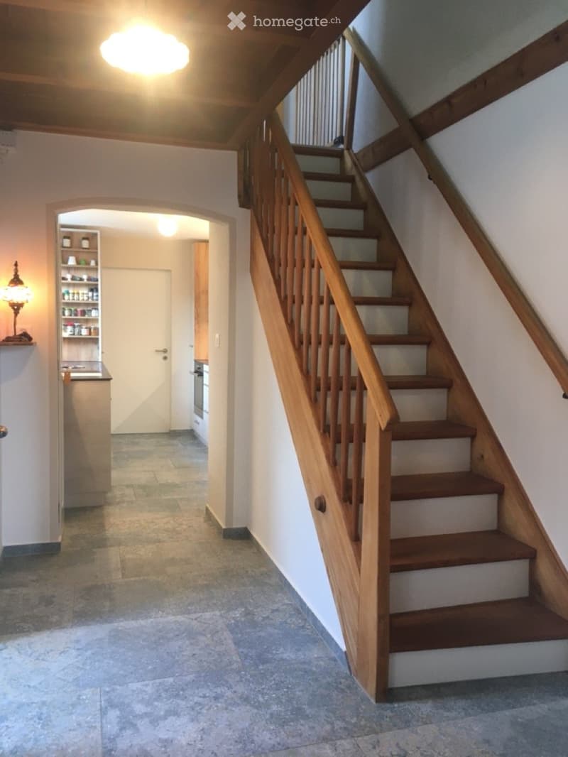 Wooden staircase with a handrail leads to an upper level, with a small shelf and lamp visible in the background.