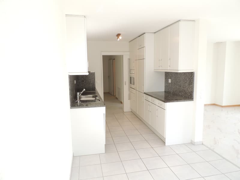 Modern kitchen with white cabinets, granite countertops, and tiled flooring. Features a sink, oven, and ample storage space.