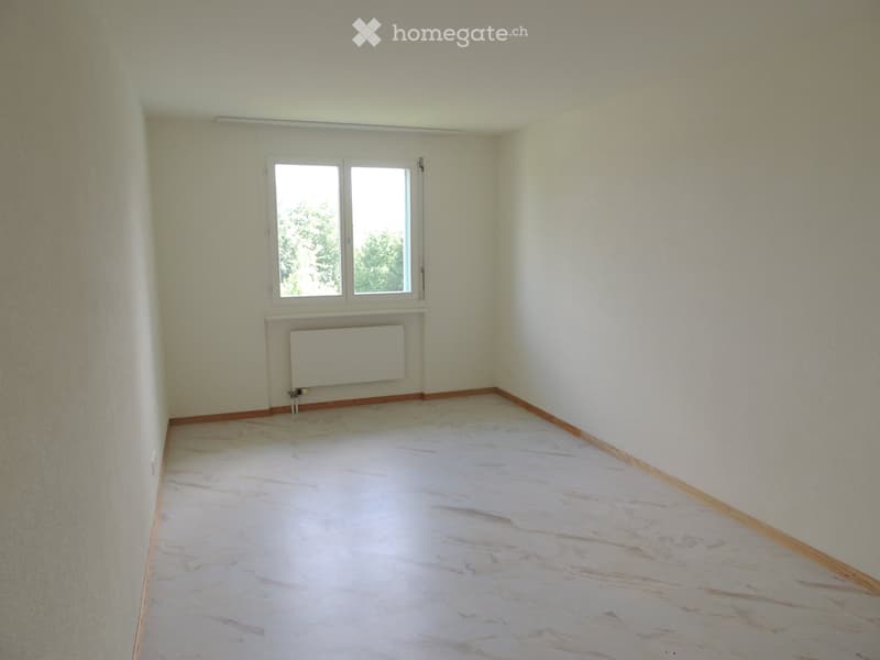 Empty room with light-colored walls, marble flooring, and a window with white frames. A radiator is mounted on the wall below the window.