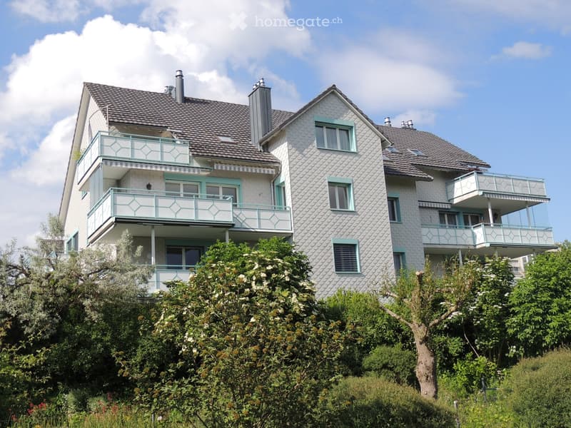 A multi-story residential building with light-colored walls, multiple balconies, and a tiled roof.