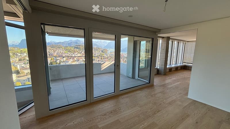 Empty room with wooden flooring, large glass sliding doors leading to a balcony with a scenic mountain view.