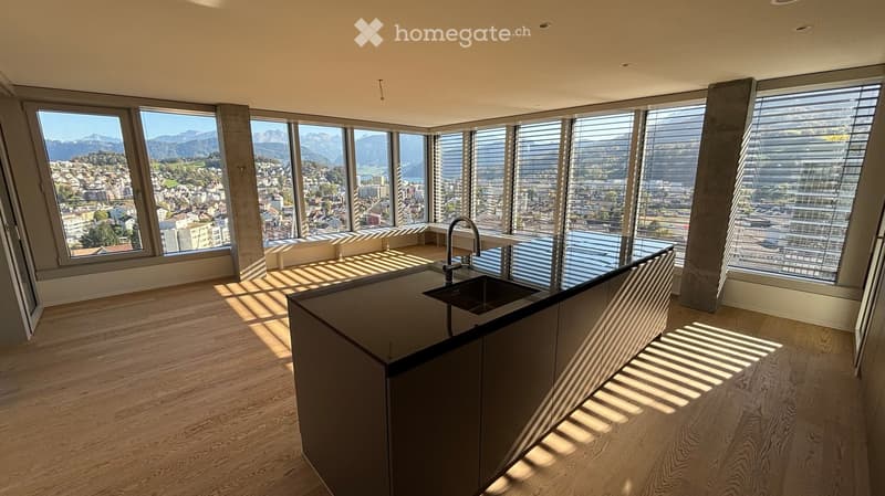 Modern kitchen with wooden flooring, large windows offering a scenic mountain view, and a sleek black countertop with a sink and faucet.