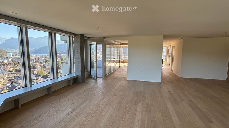 Empty room with wooden flooring, large windows offering a scenic view, and a bench near the window.