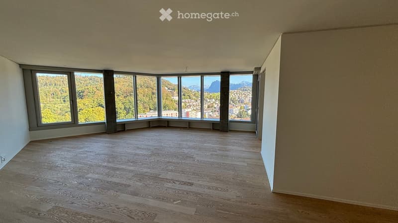 Empty room with wooden flooring and large windows offering a scenic view of a town and mountains.
