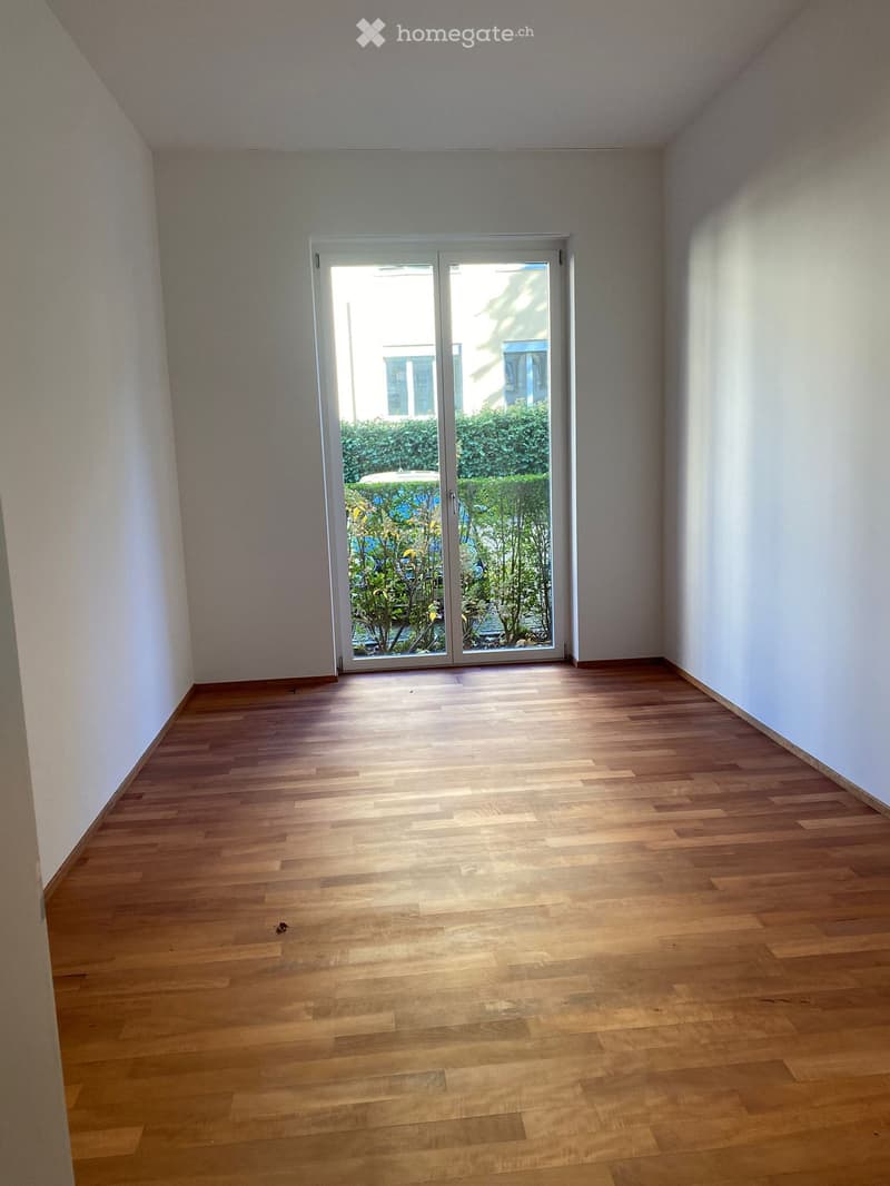 empty room with wooden floor, sliding doors, glass walls, and shrubs in the garden