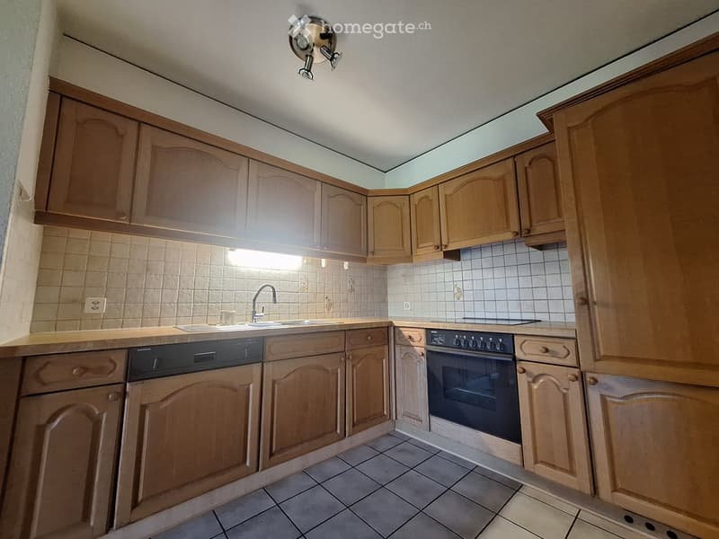 Well-lit kitchen with wooden cabinets, tiled walls, and modern appliances including a sink, oven, and dishwasher.