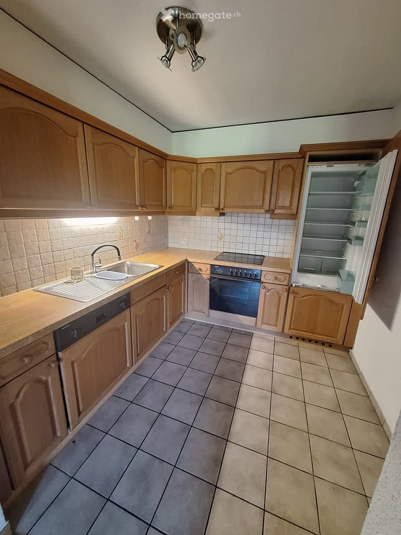 Well-lit kitchen with wooden cabinets, tiled floor, sink, oven, refrigerator, and dishwasher.