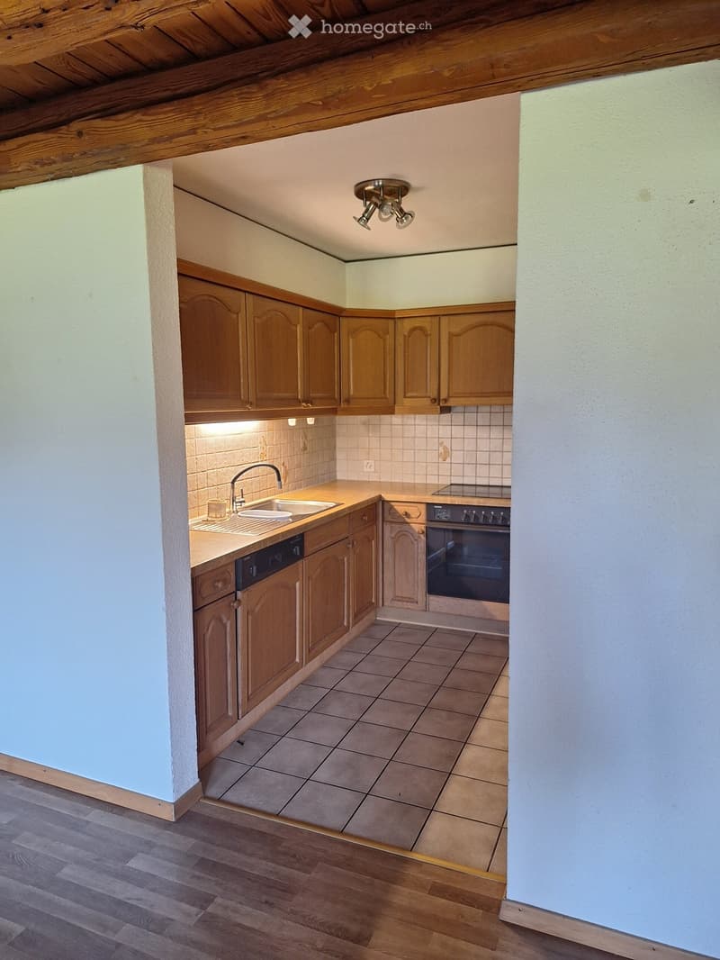 Modern kitchen with wooden cabinets, stainless steel sink, oven, and dishwasher. Light-colored tiles and wooden flooring.